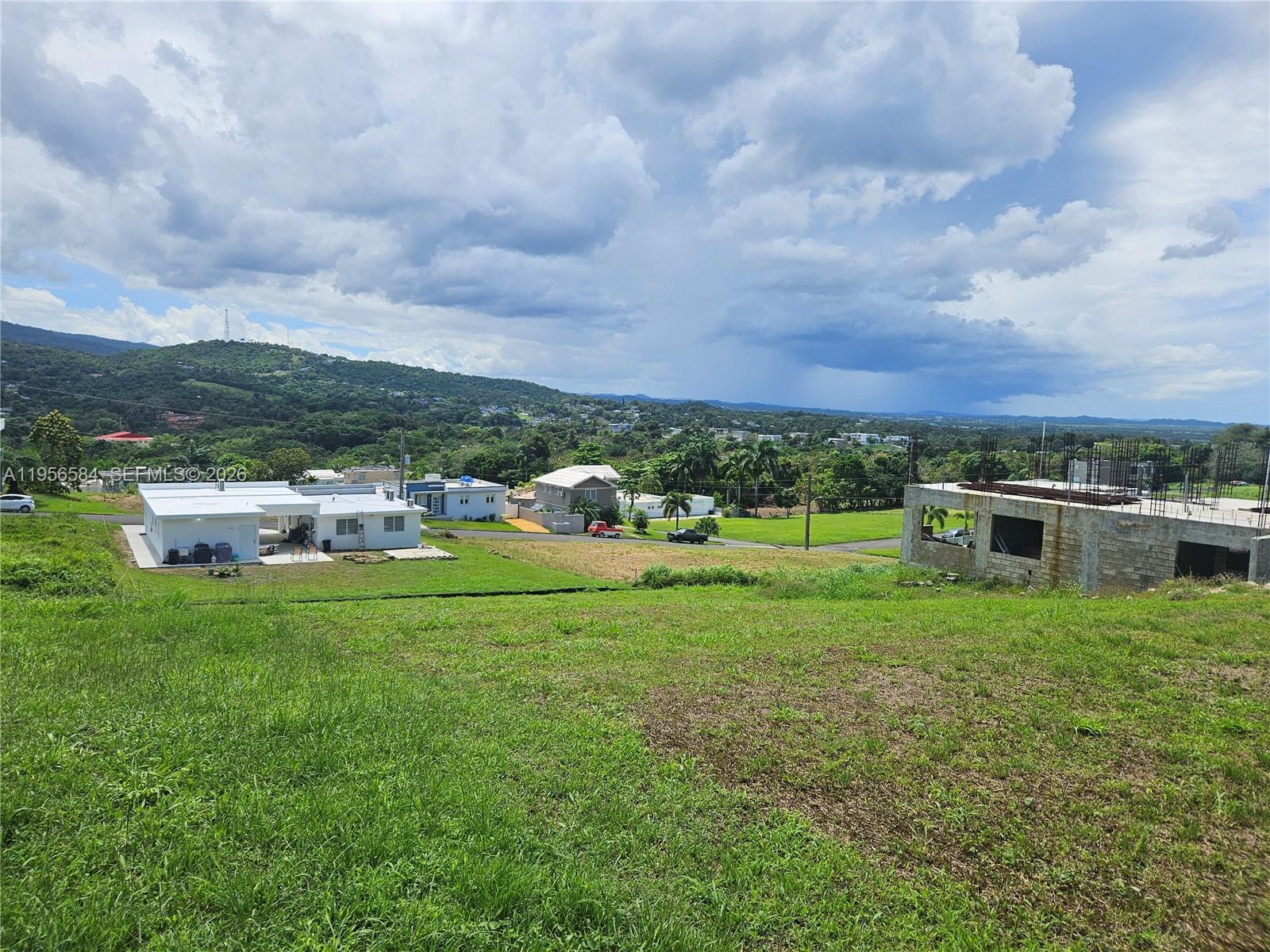 An elevated view shows a grassy lot overlooking a residential area with houses and construction — URB MIRADOR DE PALMER . SOLAR 41 RIO GRANDE, PR 00745, PR