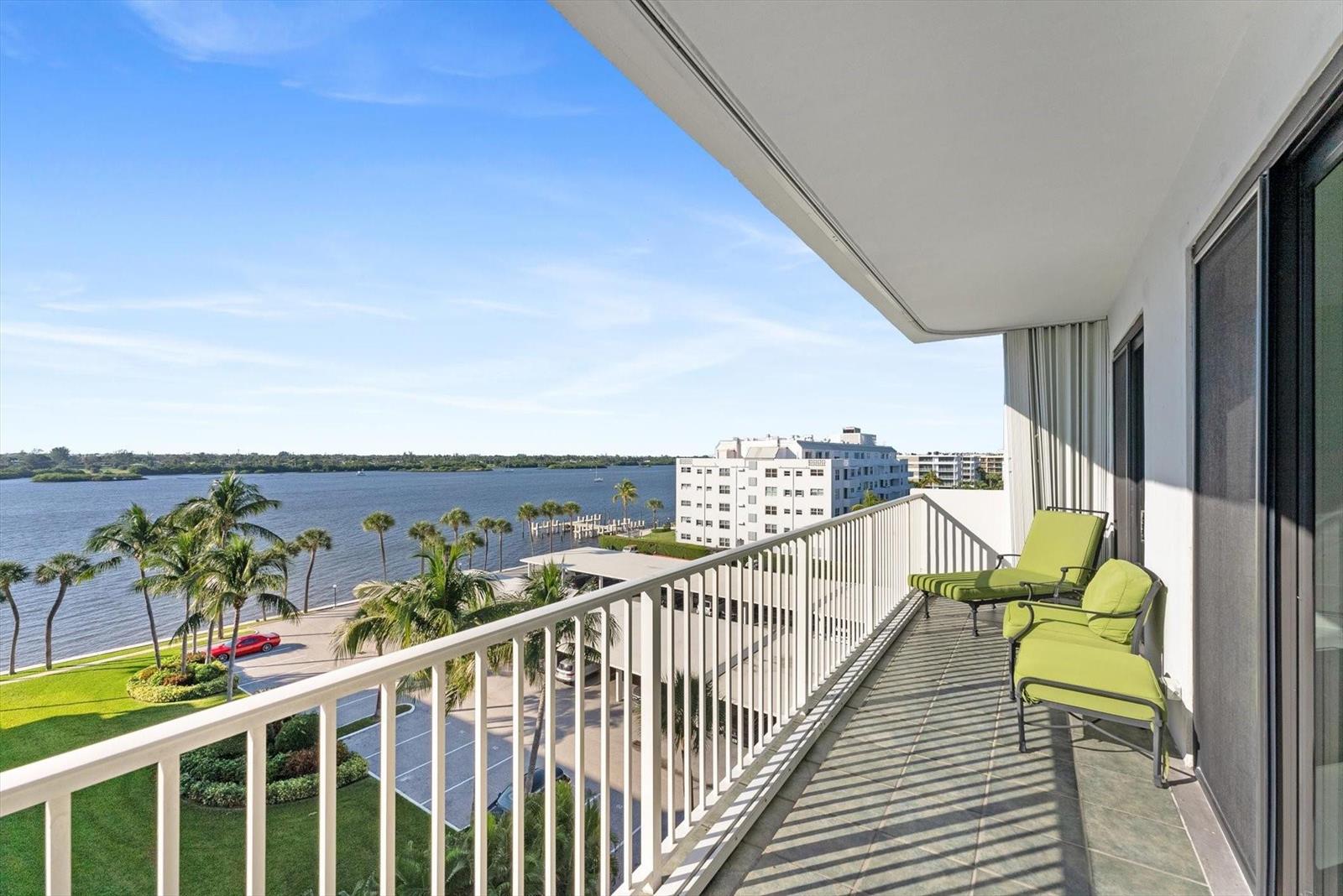 A balcony with green lounge chairs overlooks a waterfront view with palm trees and buildings — 2860 S Ocean Boulevard # 601, Palm Beach FL 33480, PALM BEACH, FL