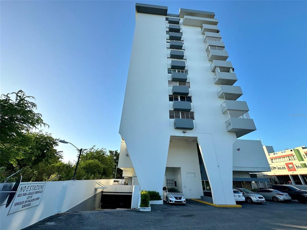 A low-angle exterior view of a white multi-story apartment building with balconies and a parking lot — 1802 ALCAZAR UNIT 404, PONCE, PR