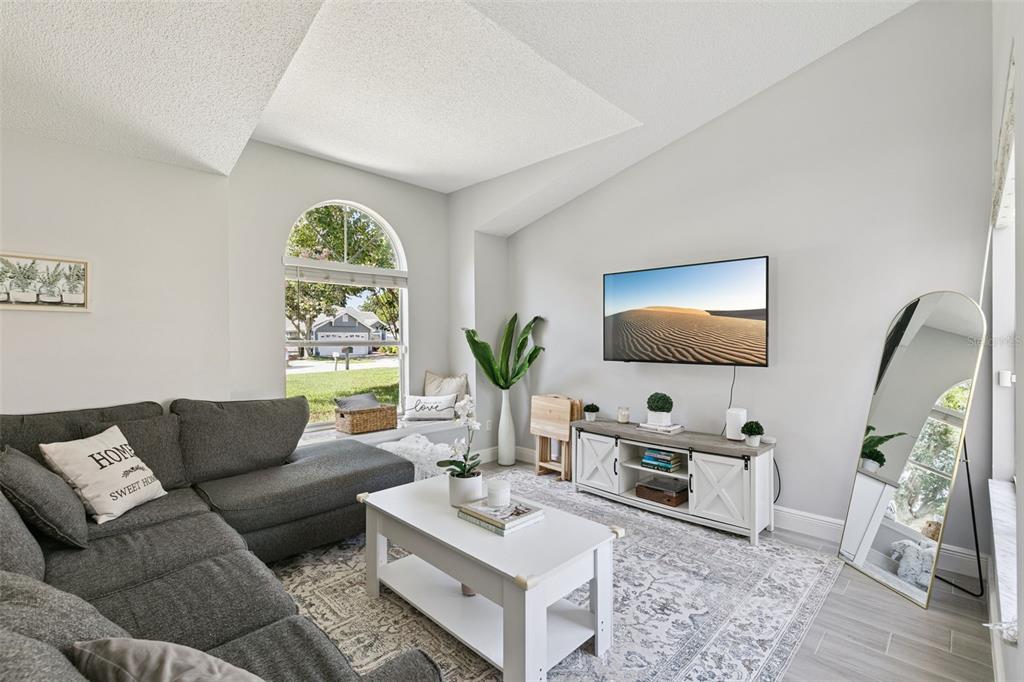 A living room features a grey sectional sofa, white coffee table, TV, and arched window — 7503 PACIFIC HEIGHTS CIRCLE, ORLANDO, FL