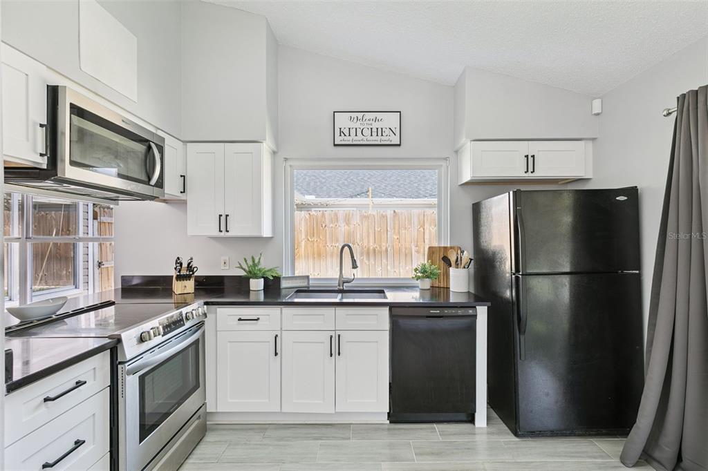 A kitchen features white cabinets, black countertops, stainless steel appliances, and a window over the sink — 7503 PACIFIC HEIGHTS CIRCLE, ORLANDO, FL