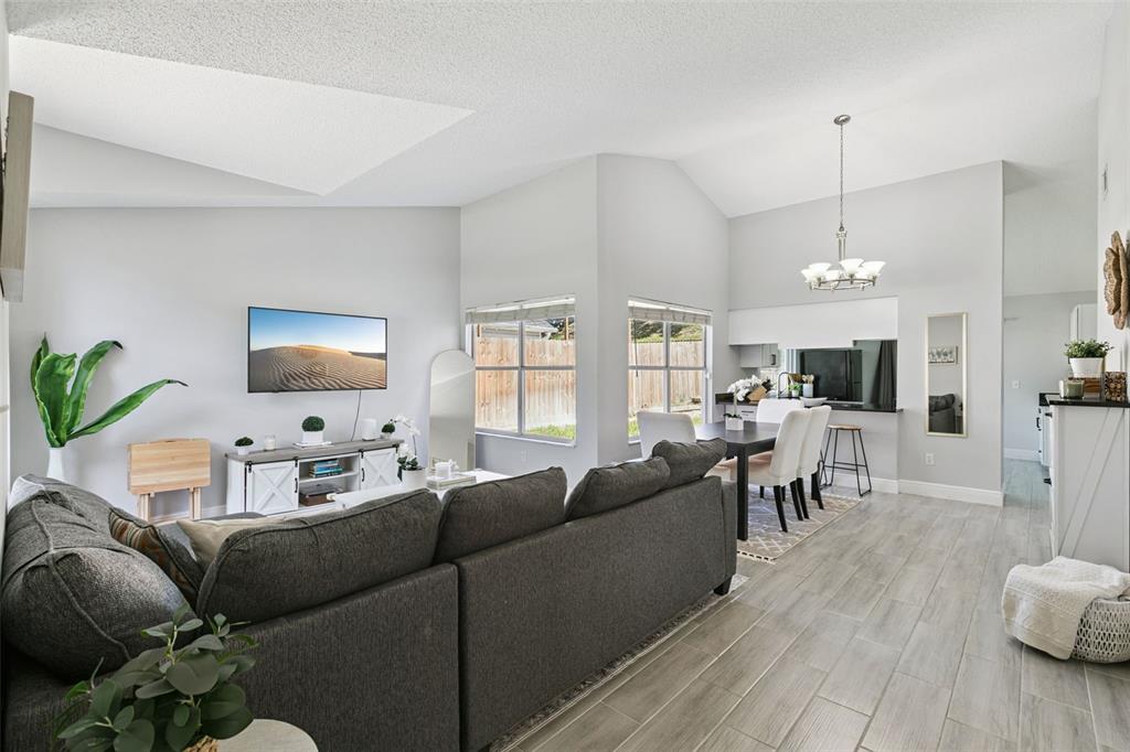 A living room and dining area with gray walls, wood-look tile flooring, and vaulted ceilings — 7503 PACIFIC HEIGHTS CIRCLE, ORLANDO, FL