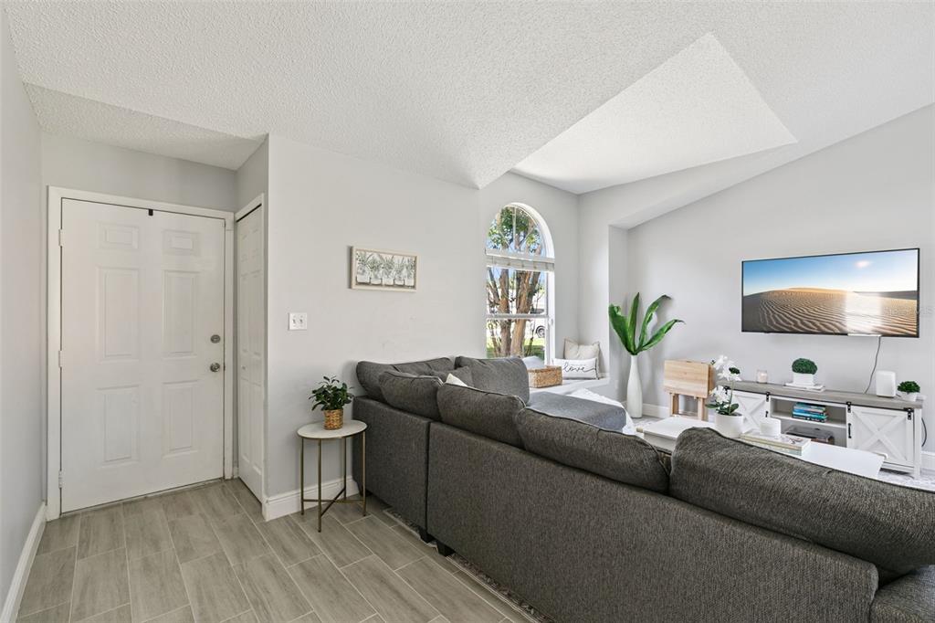 A living room features gray tile flooring, a sectional sofa, and a vaulted ceiling — 7503 PACIFIC HEIGHTS CIRCLE, ORLANDO, FL