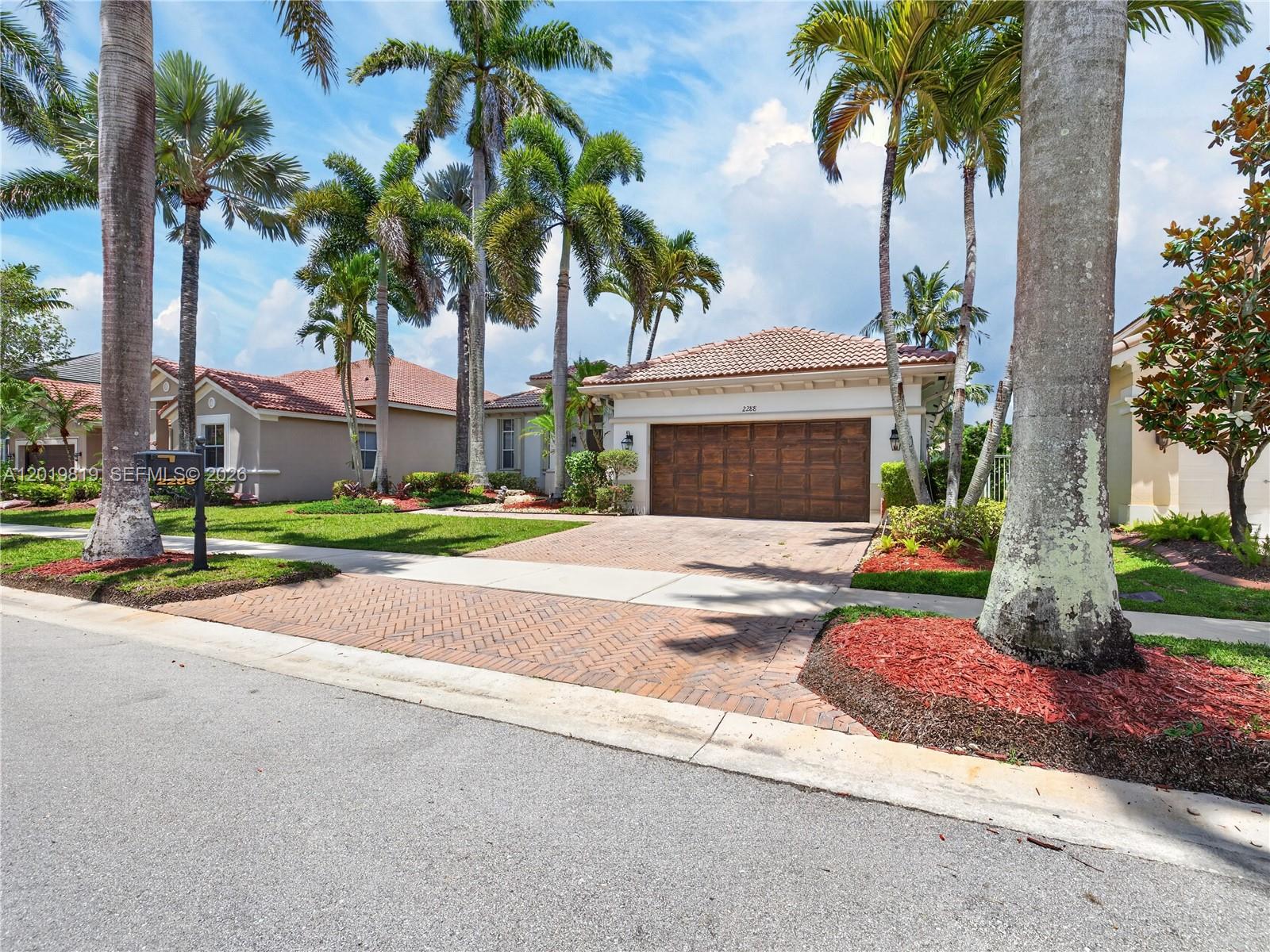 A single-story house with a tiled roof, wooden garage door, and palm trees in front — 2288 Quail Roost Dr, Weston FL 33327, WESTON, FL