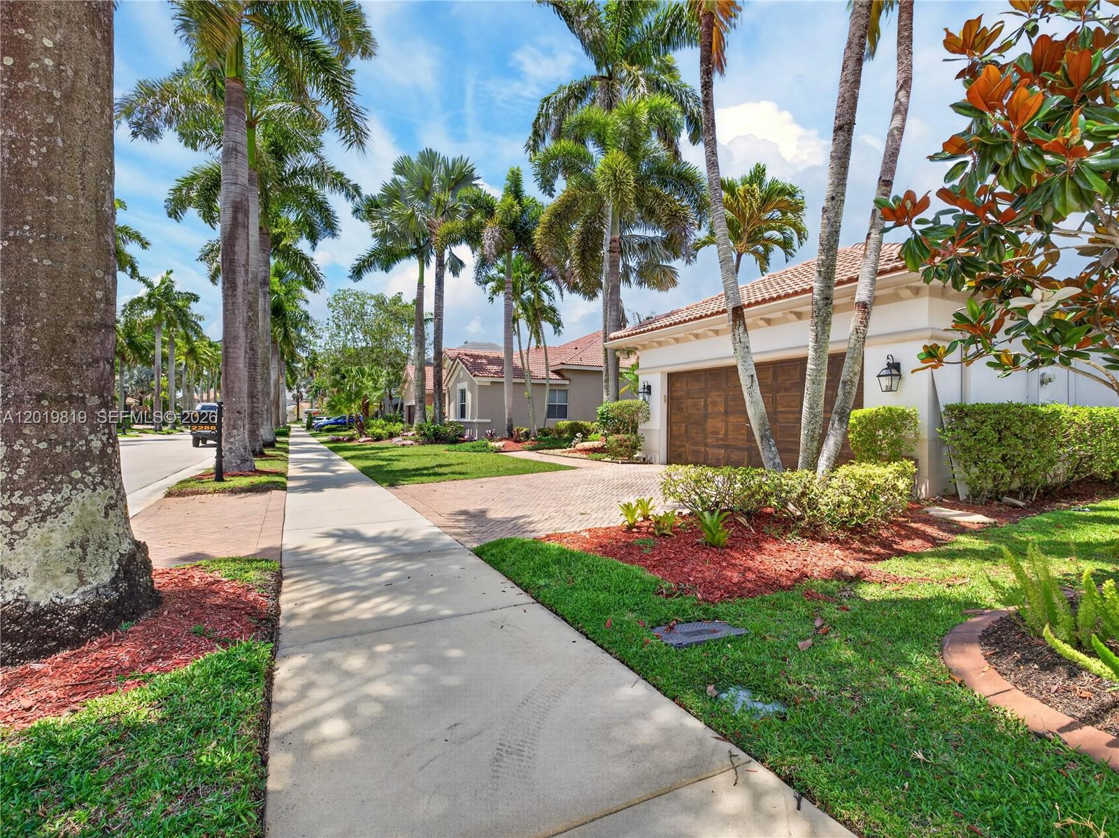 A sidewalk leads past a suburban house with a brick driveway and palm trees — 2288 Quail Roost Dr, Weston FL 33327, WESTON, FL