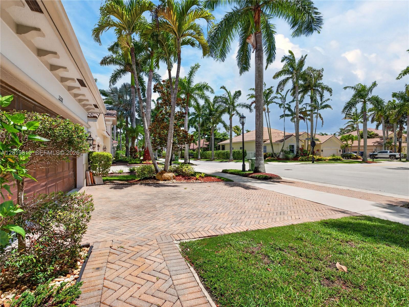 A paved driveway leads to a garage beside a street lined with palm trees — 2288 Quail Roost Dr, Weston FL 33327, WESTON, FL