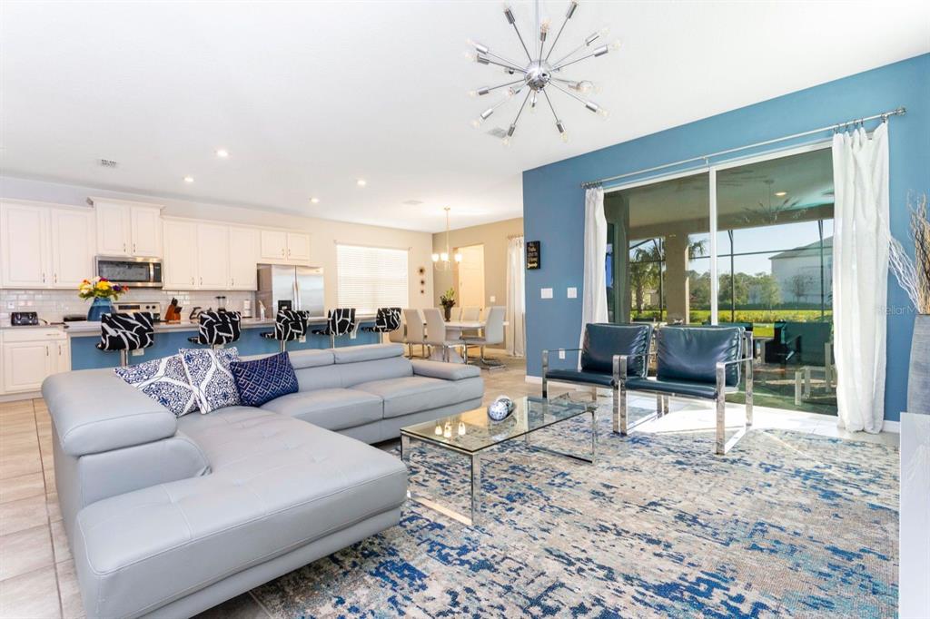 A modern open-concept living room and kitchen featuring a grey sectional, blue accent wall, and chandelier — 8995 AMELIA DOWNS TRAIL, KISSIMMEE, FL