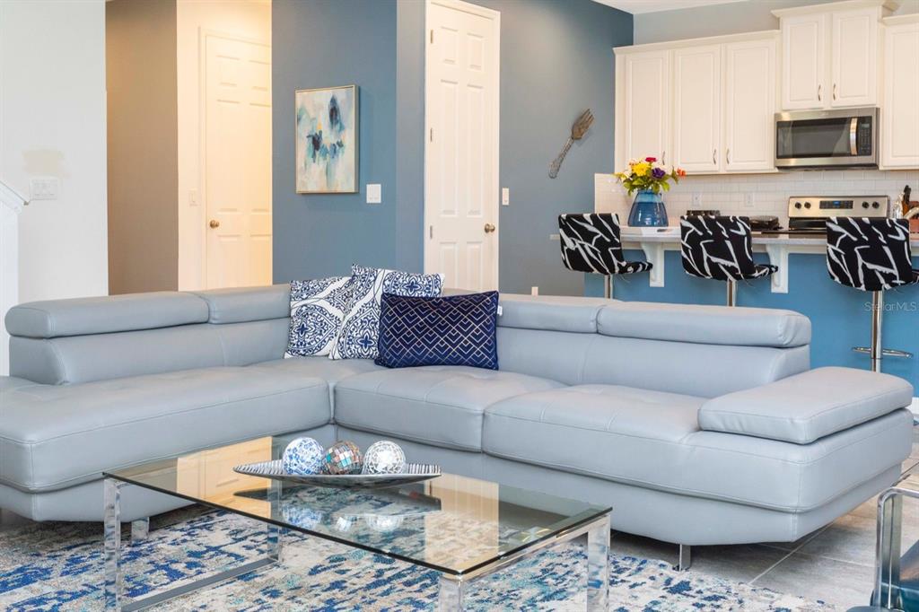 A light blue sectional sofa sits in a living room facing a kitchen with barstools — 8995 AMELIA DOWNS TRAIL, KISSIMMEE, FL