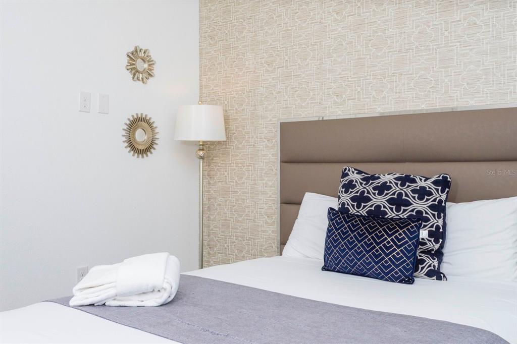 A bedroom features a bed with patterned pillows, a floor lamp, and textured wallpaper — 8995 AMELIA DOWNS TRAIL, KISSIMMEE, FL