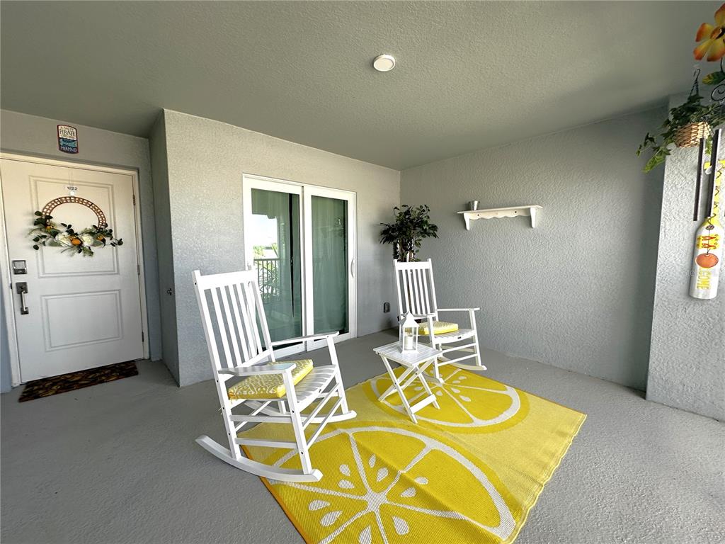 A covered patio features two white rocking chairs on a lemon-patterned rug — 14267 HERITAGE LANDING BOULEVARD UNIT 1222, PUNTA GORDA, FL