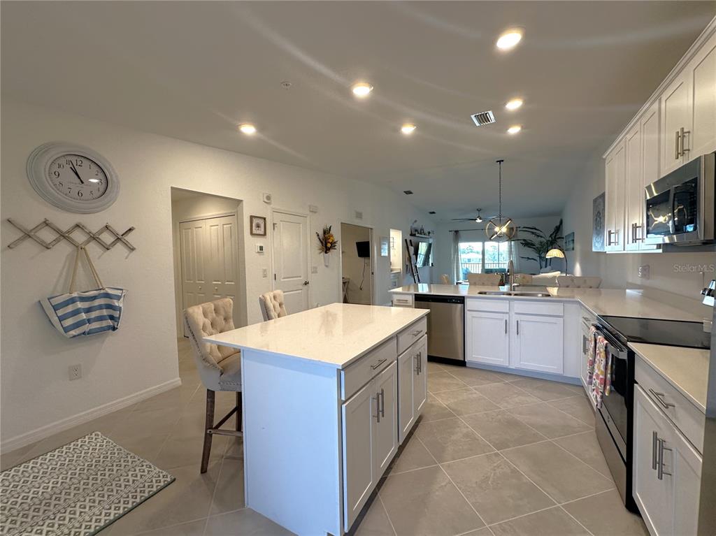A modern kitchen features white cabinets, a quartz-topped island, and light-colored tile flooring — 14267 HERITAGE LANDING BOULEVARD UNIT 1222, PUNTA GORDA, FL