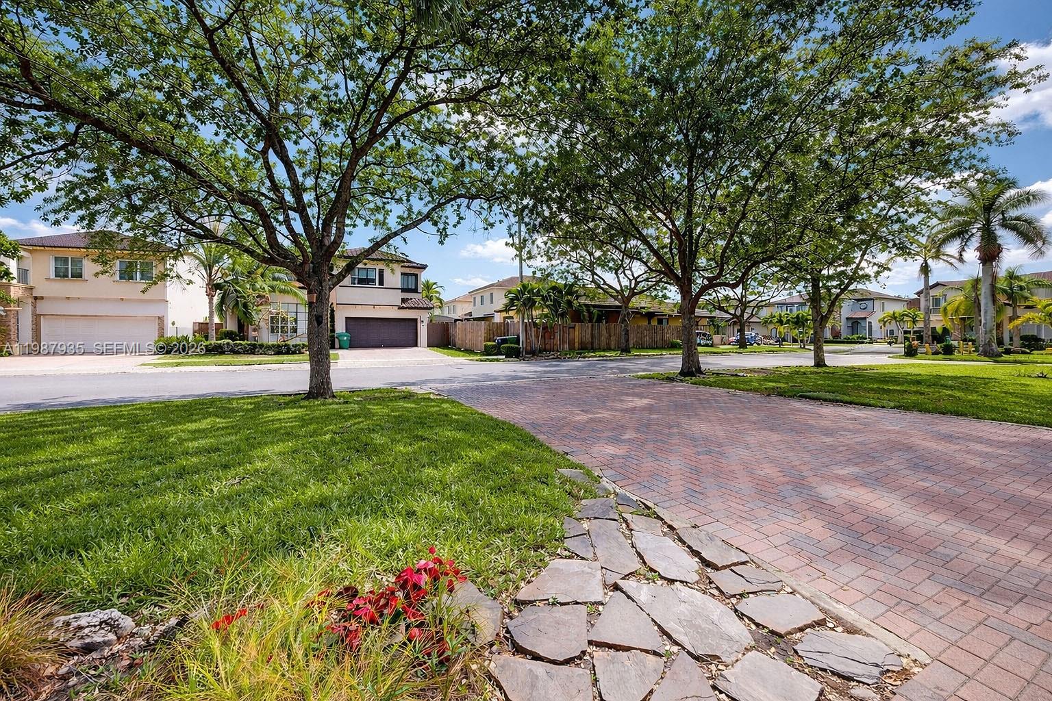 A paved driveway leads toward houses surrounded by mature trees and green lawns — 16479 SW 50th Ter, Miami FL 33185, MIAMI, FL