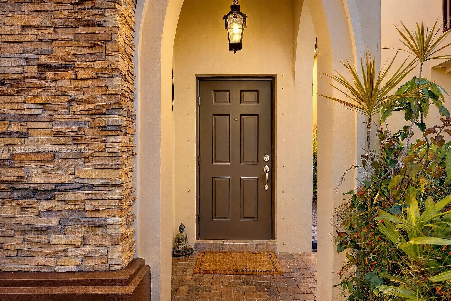 A brown front door is set within a stone-accented arched entryway with a small statue — 16479 SW 50th Ter, Miami FL 33185, MIAMI, FL