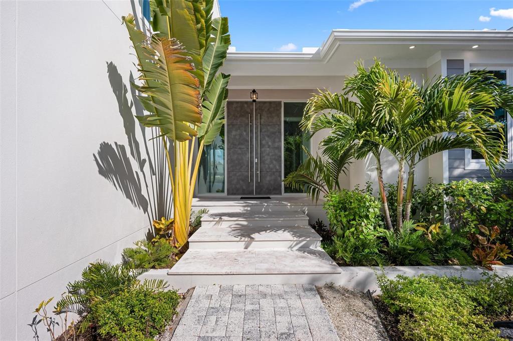 A modern home entrance features stone steps, double doors, and lush tropical landscaping — 4819 HIGEL AVENUE, SARASOTA, FL
