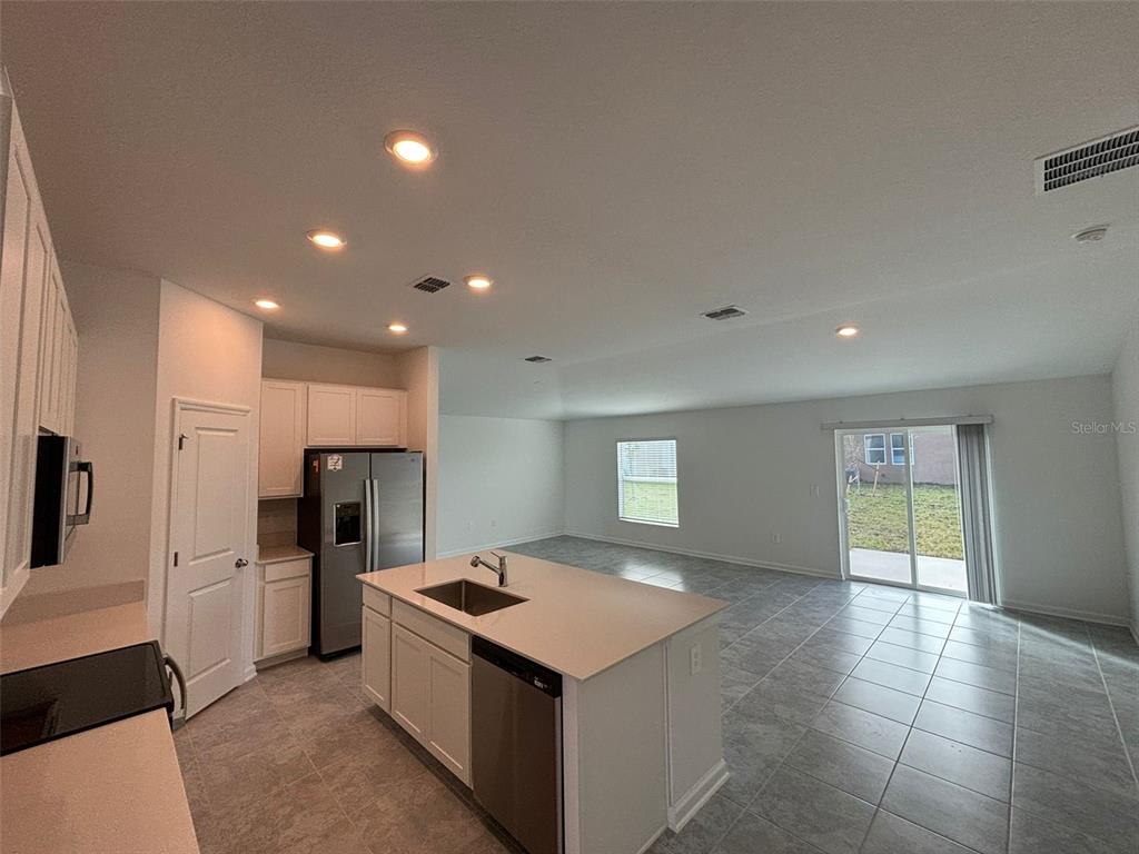 A kitchen with white cabinets and a center island opens into a tiled living area — 655 DARING DRIVE, DAVENPORT, FL
