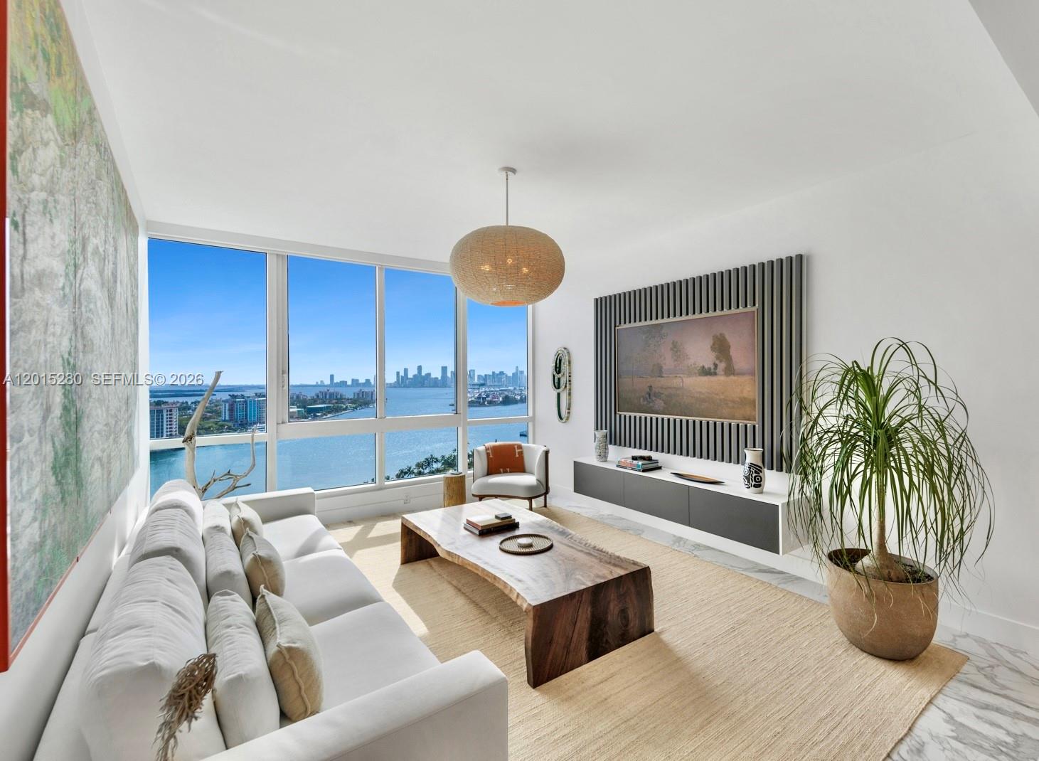A modern living room features a live-edge coffee table, a wall-mounted television, and waterfront views — 100 S Pointe Dr # 2003, Miami Beach FL 33139, MIAMI BEACH, FL