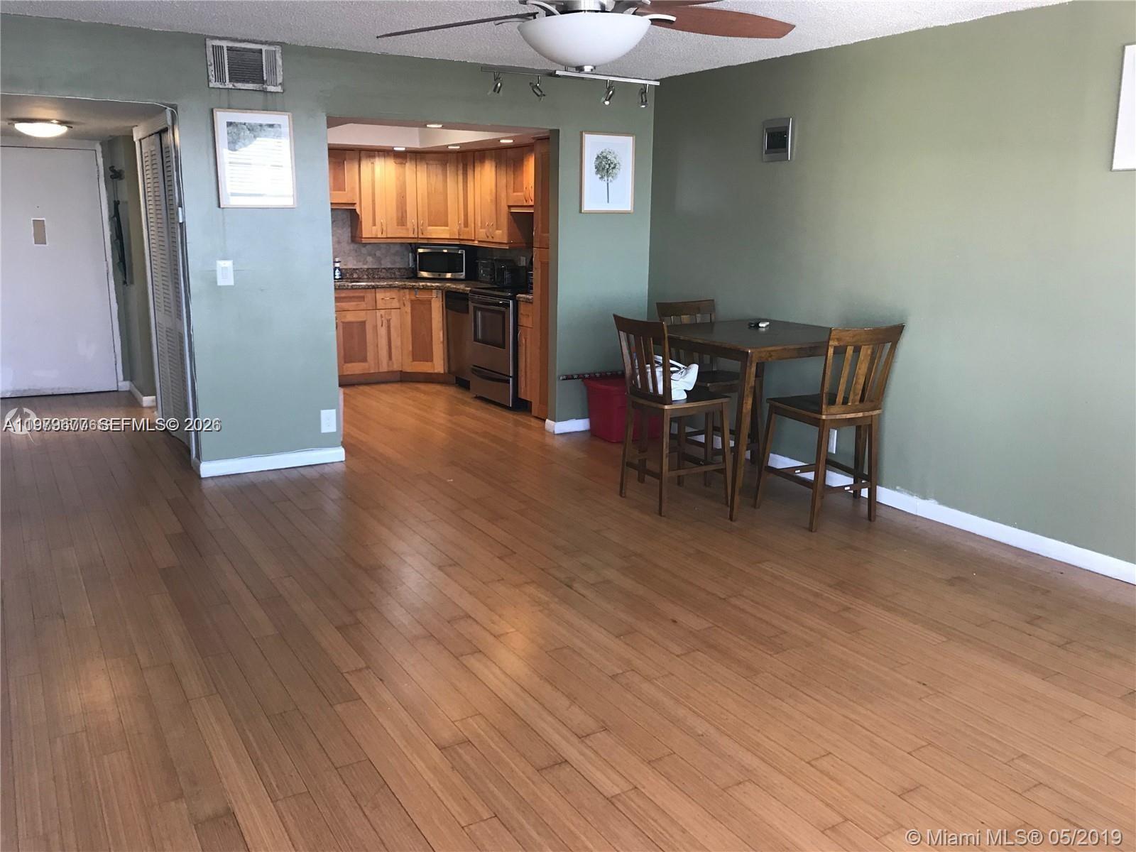 An open-concept dining area with wood flooring leads into a kitchen with wooden cabinets — 2025 NE 164th St # 1015, North Miami Beach FL 33162, NORTH MIAMI BEACH, FL