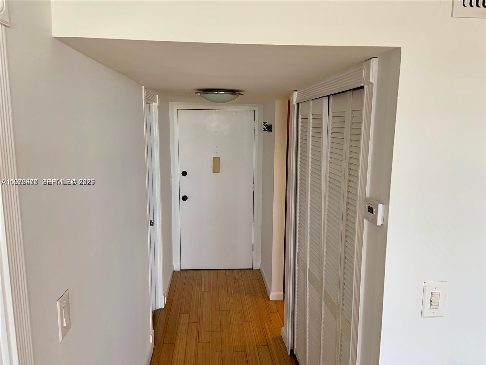 A hallway features wood-look flooring, a white entry door, and a louvered closet door — 2025 NE 164th St # 1015, North Miami Beach FL 33162, NORTH MIAMI BEACH, FL