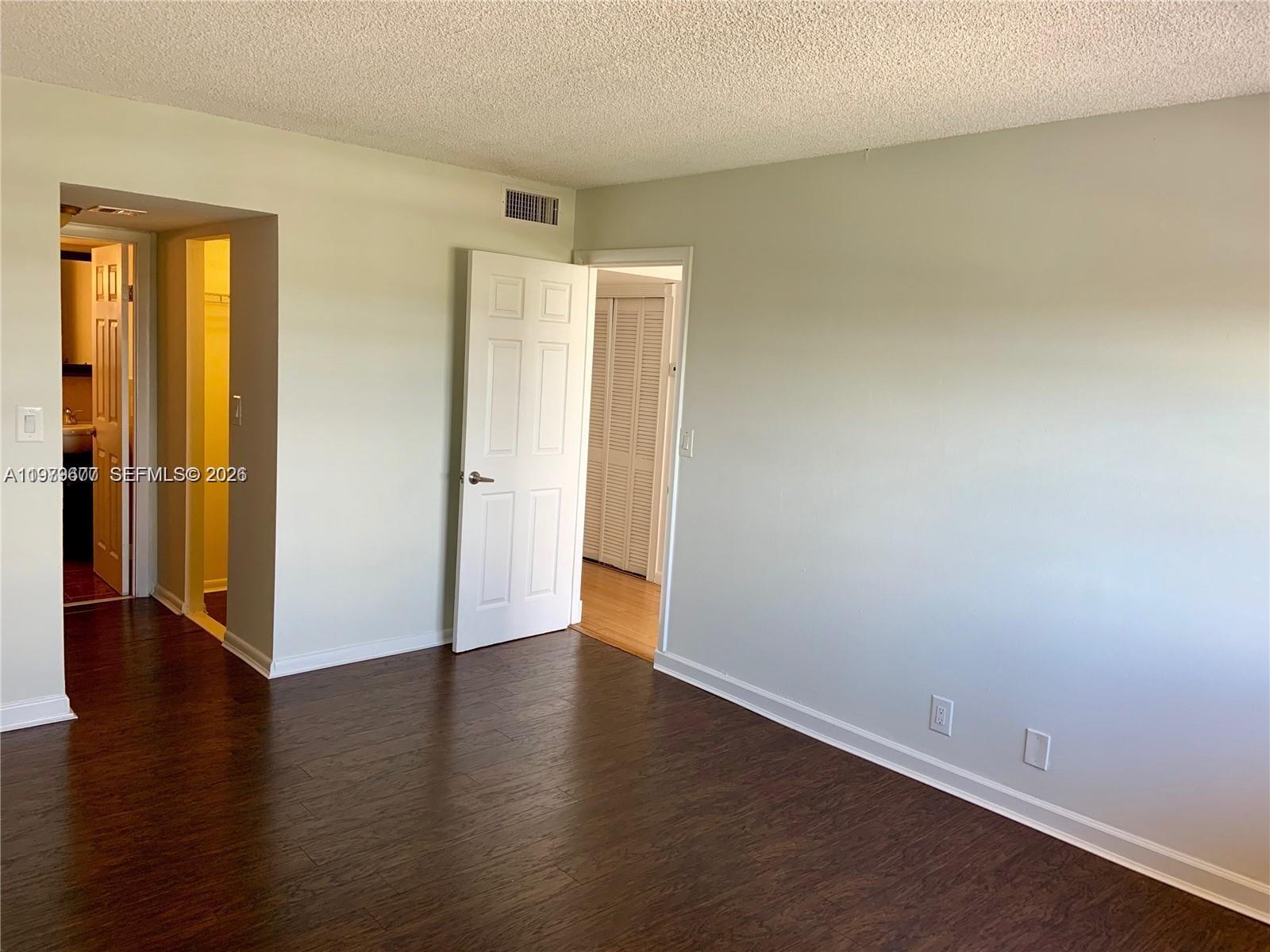 An interior room features dark wood-look flooring, light-colored walls, and two open doorways — 2025 NE 164th St # 1015, North Miami Beach FL 33162, NORTH MIAMI BEACH, FL