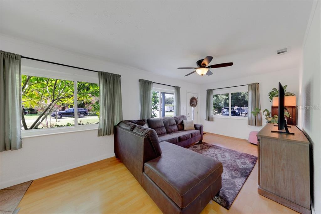 A living room features a brown sectional sofa, hardwood floors, and windows with green curtains — 2773 BELLE HAVEN DRIVE, CLEARWATER, FL