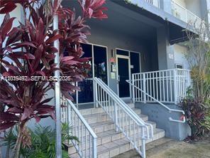 A set of concrete stairs with white railings leads to the glass entrance of a building — 2734 Bird Ave # 114, Miami FL 33133, MIAMI, FL