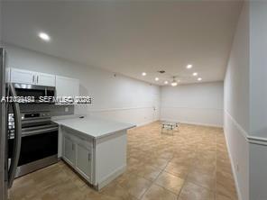 A kitchen with white cabinets and stainless steel appliances opens into a spacious tiled room — 2734 Bird Ave # 114, Miami FL 33133, MIAMI, FL