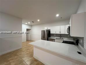 A kitchen features white cabinets, stainless steel appliances, and a white quartz breakfast bar — 2734 Bird Ave # 114, Miami FL 33133, MIAMI, FL
