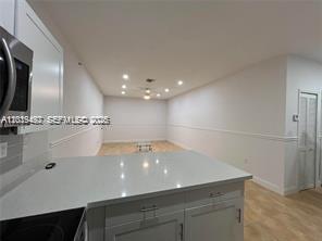 A kitchen with white cabinets and a quartz countertop overlooks an empty living area — 2734 Bird Ave # 114, Miami FL 33133, MIAMI, FL