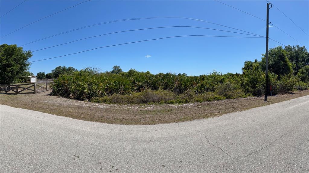 A vacant, overgrown corner lot is bordered by paved roads and a wooden fence — Lot 22 AMERICANA AVENUE, NORTH PORT, FL