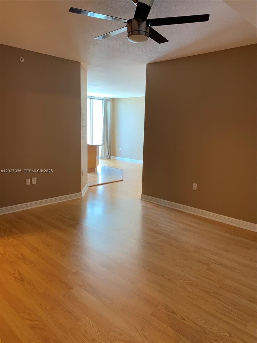 An interior view shows a room with light wood flooring, tan walls, and a ceiling fan — HALLANDALE BEACH, FL