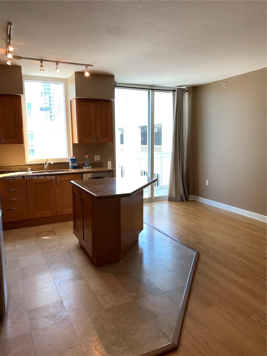 A kitchen with wood cabinets and a stone island transitions to a wood-floored living area — HALLANDALE BEACH, FL