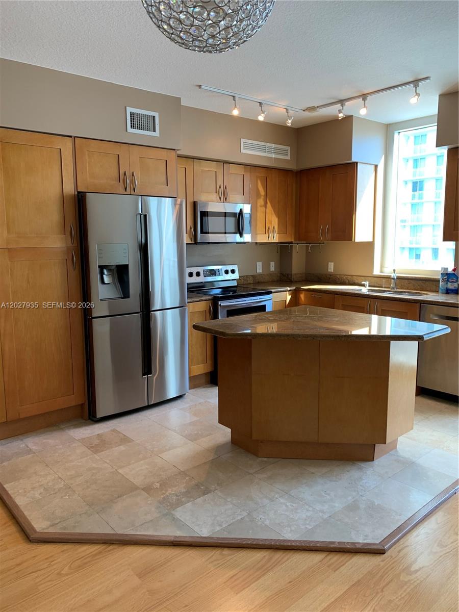 A kitchen features light wood cabinets, stainless steel appliances, a granite island, and tile flooring — HALLANDALE BEACH, FL
