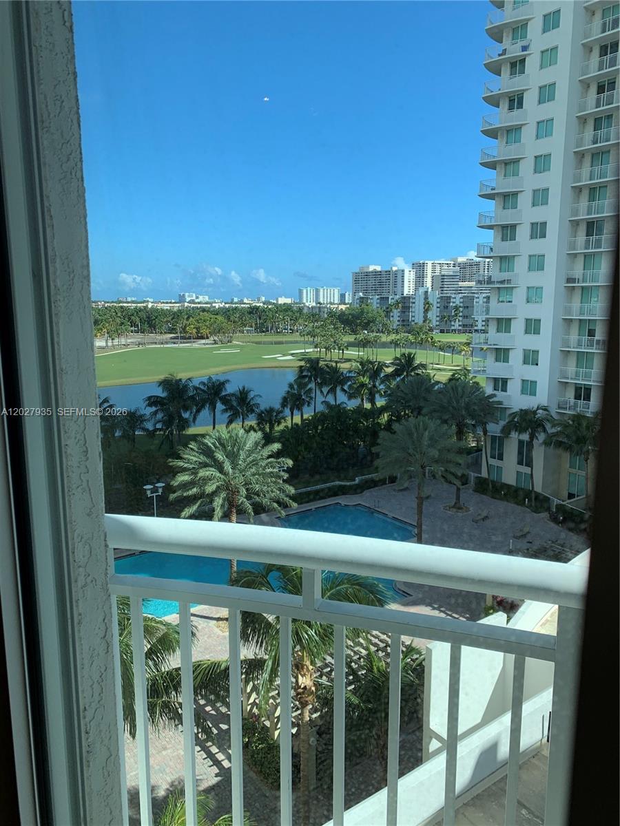 A balcony view overlooks a swimming pool, a golf course, and a high-rise building — HALLANDALE BEACH, FL