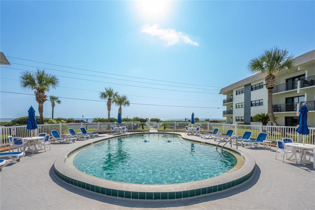 An outdoor swimming pool with lounge chairs and umbrellas sits before a multi-story apartment building — 2100 OCEAN SHORE BOULEVARD UNIT 1150, ORMOND BEACH, FL
