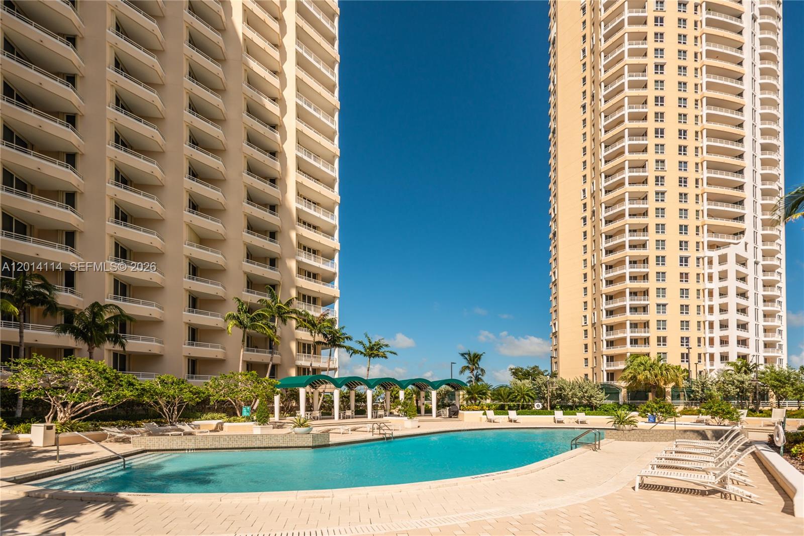 A swimming pool sits between two tall residential towers with balconies under a clear sky — 888 Brickell Key Dr # 211, Miami FL 33131, MIAMI, FL