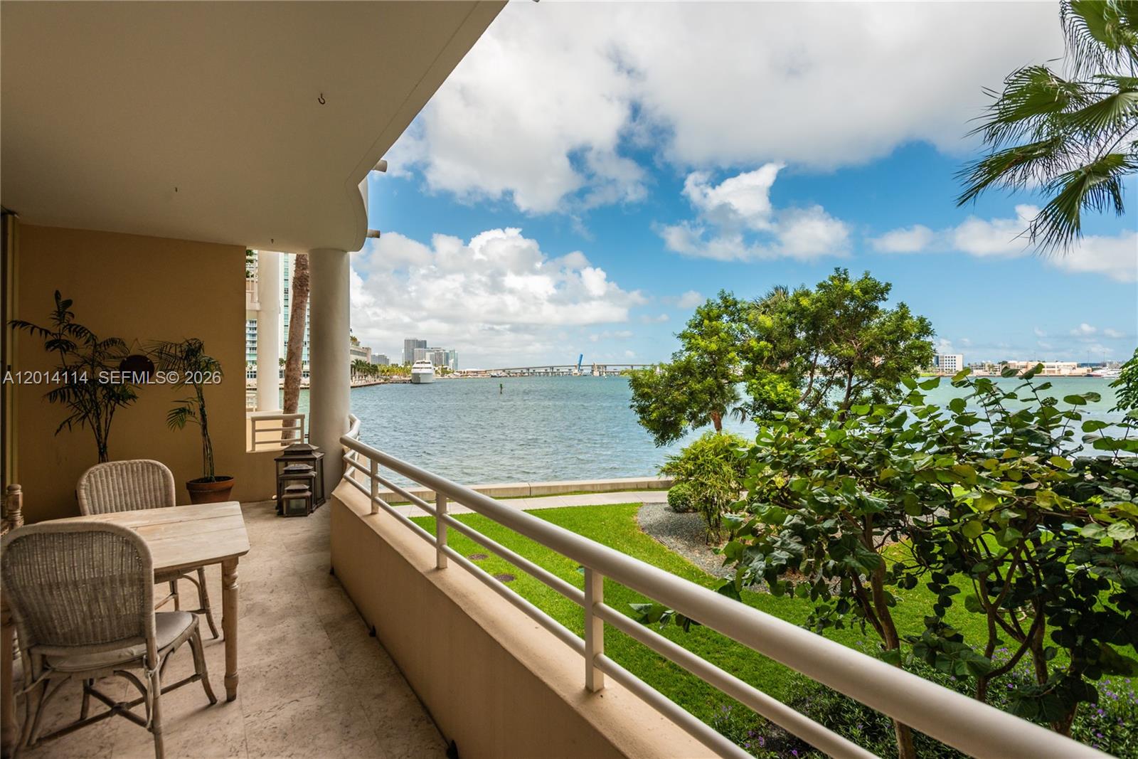 A covered balcony features a dining set overlooking a grassy lawn, trees, and the ocean — 888 Brickell Key Dr # 211, Miami FL 33131, MIAMI, FL