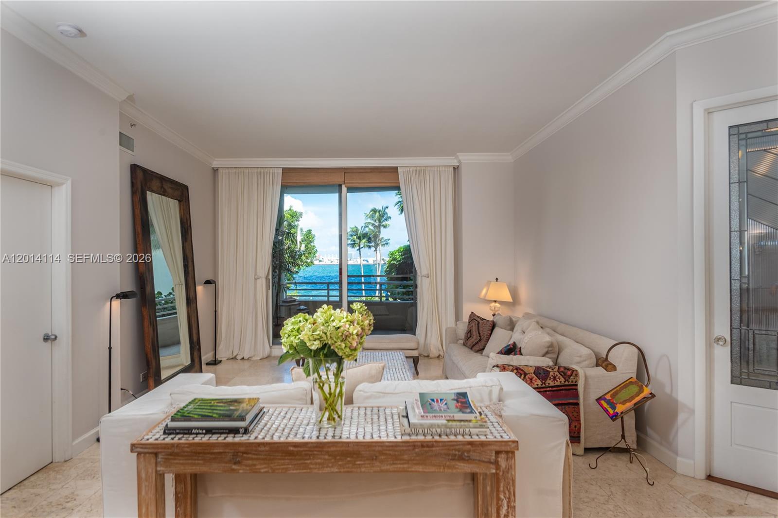 A living room features a white sofa, a wooden console table, and a balcony overlooking water — 888 Brickell Key Dr # 211, Miami FL 33131, MIAMI, FL