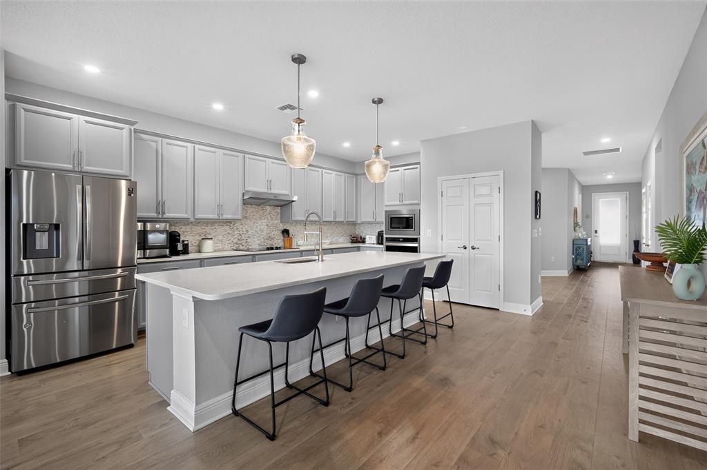 A modern open-concept kitchen features gray cabinets, a large island with bar seating, and hardwood floors — 8612 ARROW CREEK DRIVE, PARRISH, FL