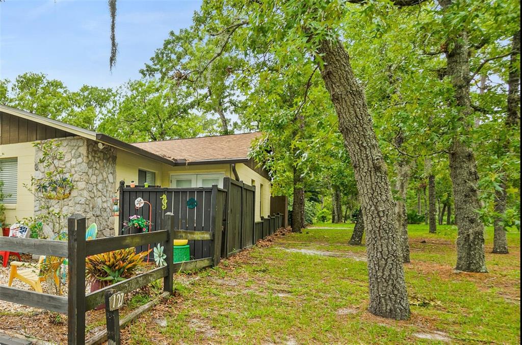 A single-story house with a stone facade and a dark wooden fence in a wooded area — 127 CYPRESS POND ROAD, PORT ORANGE, FL