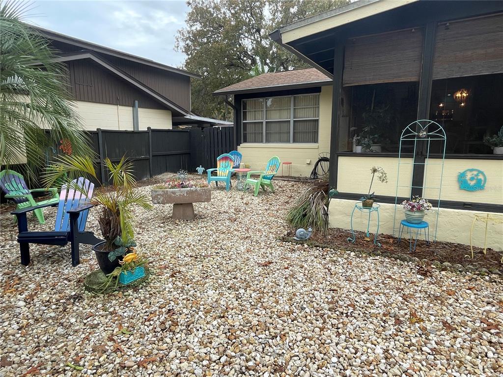 A backyard features a gravel ground, several colorful Adirondack chairs, and a screened-in porch — 127 CYPRESS POND ROAD, PORT ORANGE, FL