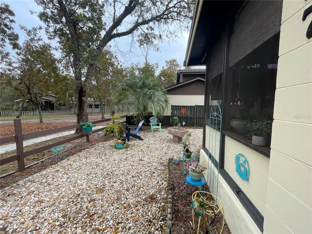 A gravel yard features a wooden fence, potted plants, and outdoor chairs beside a house — 127 CYPRESS POND ROAD, PORT ORANGE, FL