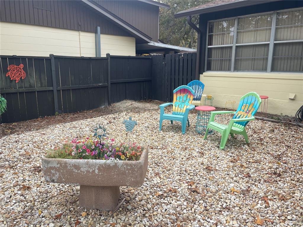 A backyard patio features gravel ground, a stone planter, and three colorful Adirondack chairs — 127 CYPRESS POND ROAD, PORT ORANGE, FL