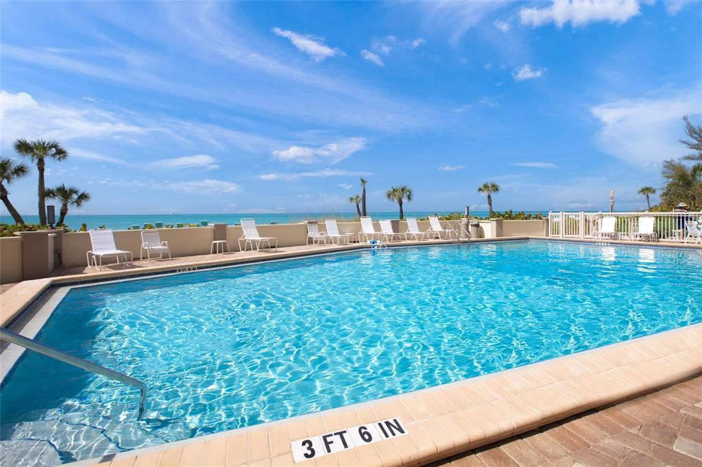 An outdoor swimming pool overlooks the ocean with lounge chairs on the surrounding deck — 101 WHISPERING SANDS DRIVE UNIT 105, SARASOTA, FL