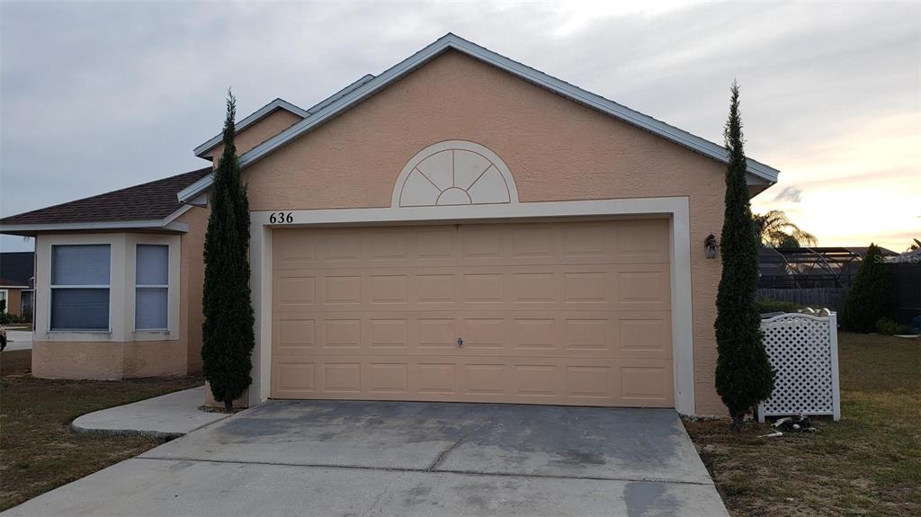 A single-story house with a peach-colored exterior, a two-car garage, and two tall evergreen trees — 636 MAJESTY DRIVE, DAVENPORT, FL