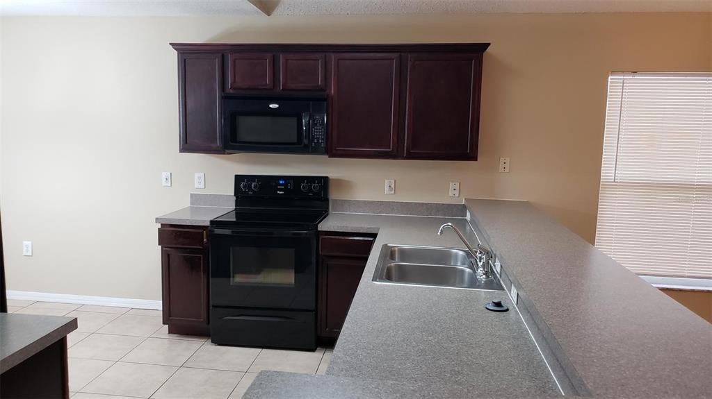A kitchen features dark wood cabinets, black appliances, a double sink, and gray countertops — 636 MAJESTY DRIVE, DAVENPORT, FL
