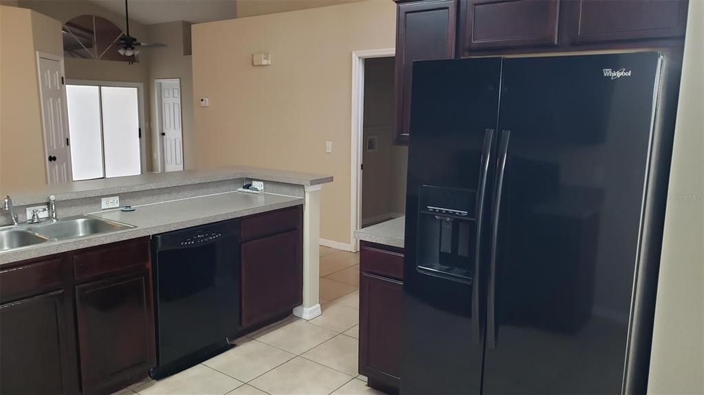 A kitchen features dark wood cabinets, a black dishwasher, a black refrigerator, and tile flooring — 636 MAJESTY DRIVE, DAVENPORT, FL