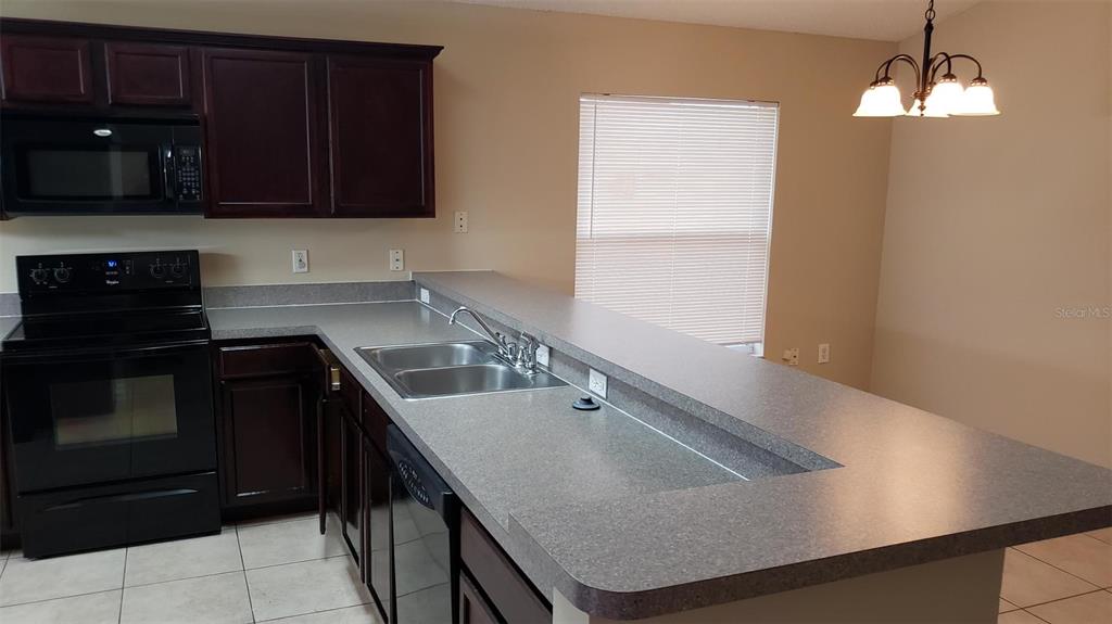A kitchen features dark wood cabinets, black appliances, gray countertops, and a breakfast bar — 636 MAJESTY DRIVE, DAVENPORT, FL