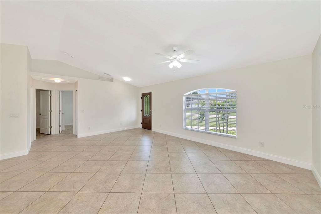 A spacious living room features light-colored tile flooring, a vaulted ceiling, and a ceiling fan — 7680 LAMPLIGHTER AVENUE, NORTH PORT, FL
