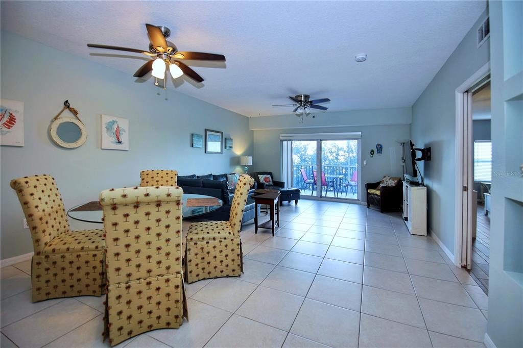 An open-concept living and dining area features tile flooring, two ceiling fans, and sliding glass doors — 5300 S ATLANTIC AVENUE UNIT 7-403, NEW SMYRNA BEACH, FL