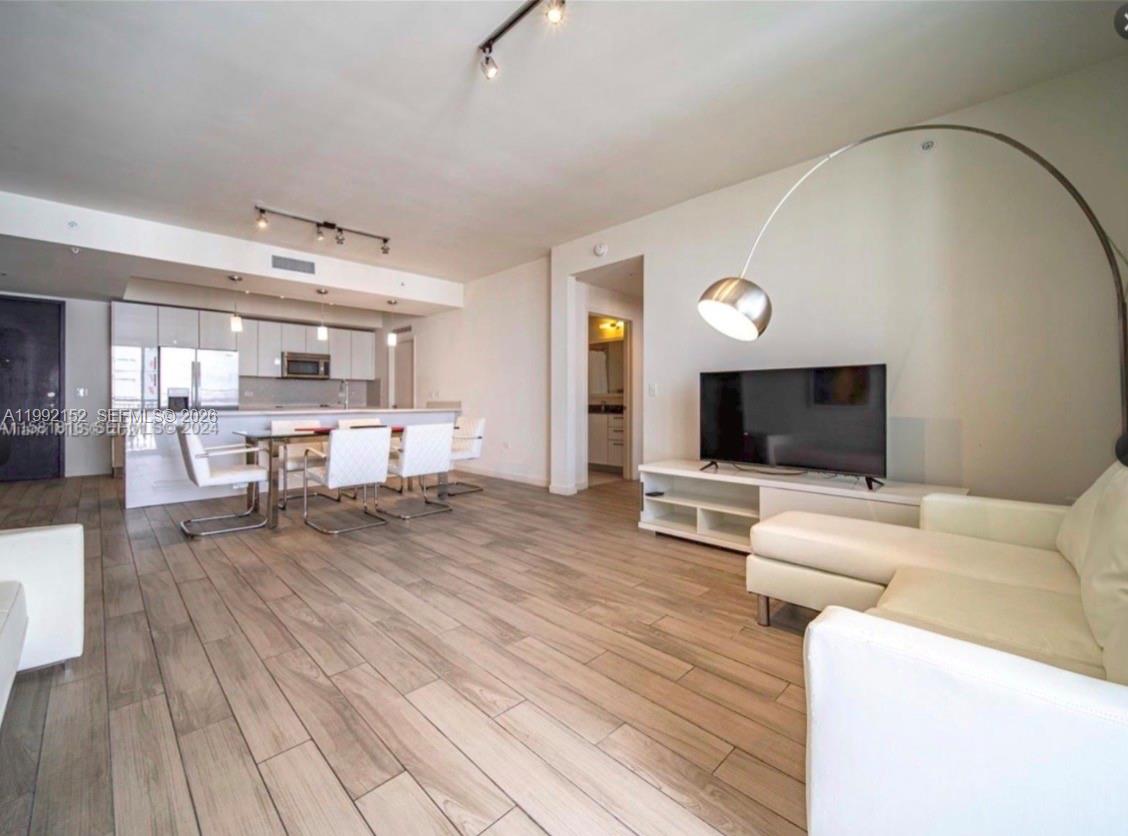 An open-concept living and dining area features white furniture, a television, and wood-look flooring — 999 SW 1st Ave # 2105, Miami FL 33130, MIAMI, FL